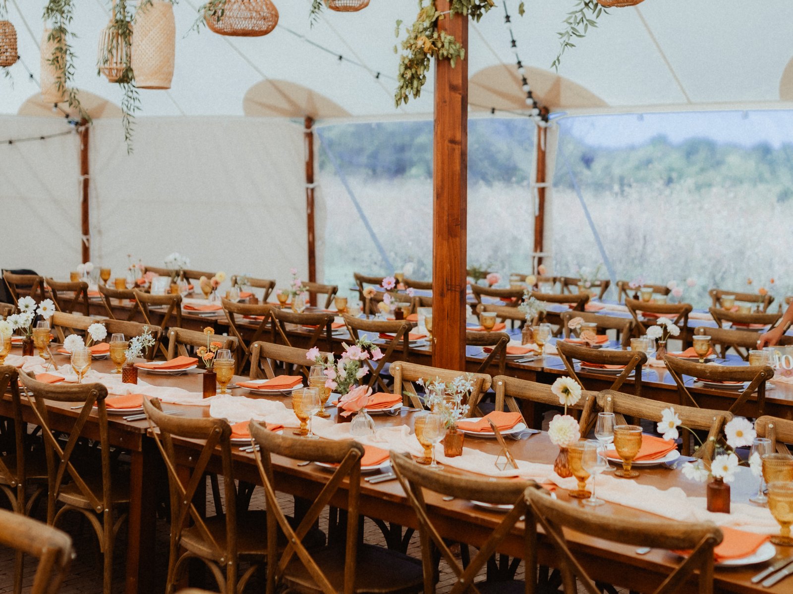 Inside the marquee: long tables and hanging lanterns facing the meadow